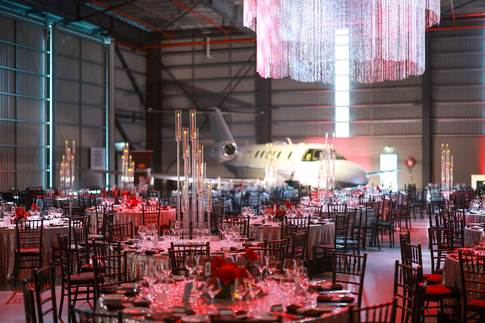 Machjet International hangar set for a gala dinner with round tables, glass candelabra and a business jet behind